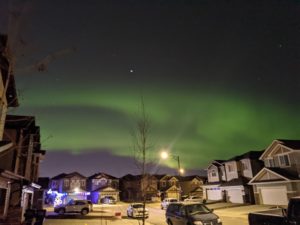 2021 balance | A picture showing a street in Edmonton with houses on every side, and on the sky above you can see the Northern Lights in a green hue.