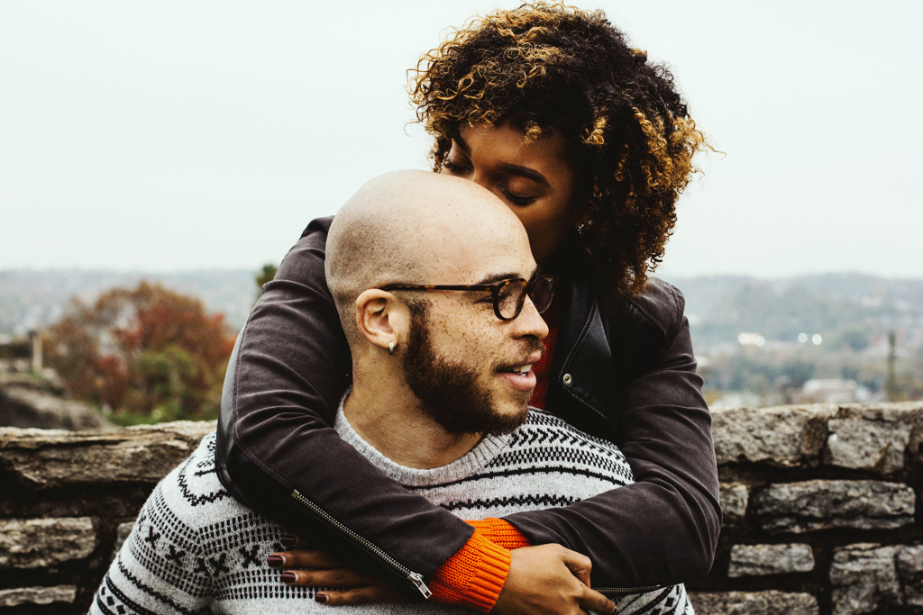 Authenticity and attachment, A photograph of a woman hugging a man from behind and kissing his head; they are outdoors.