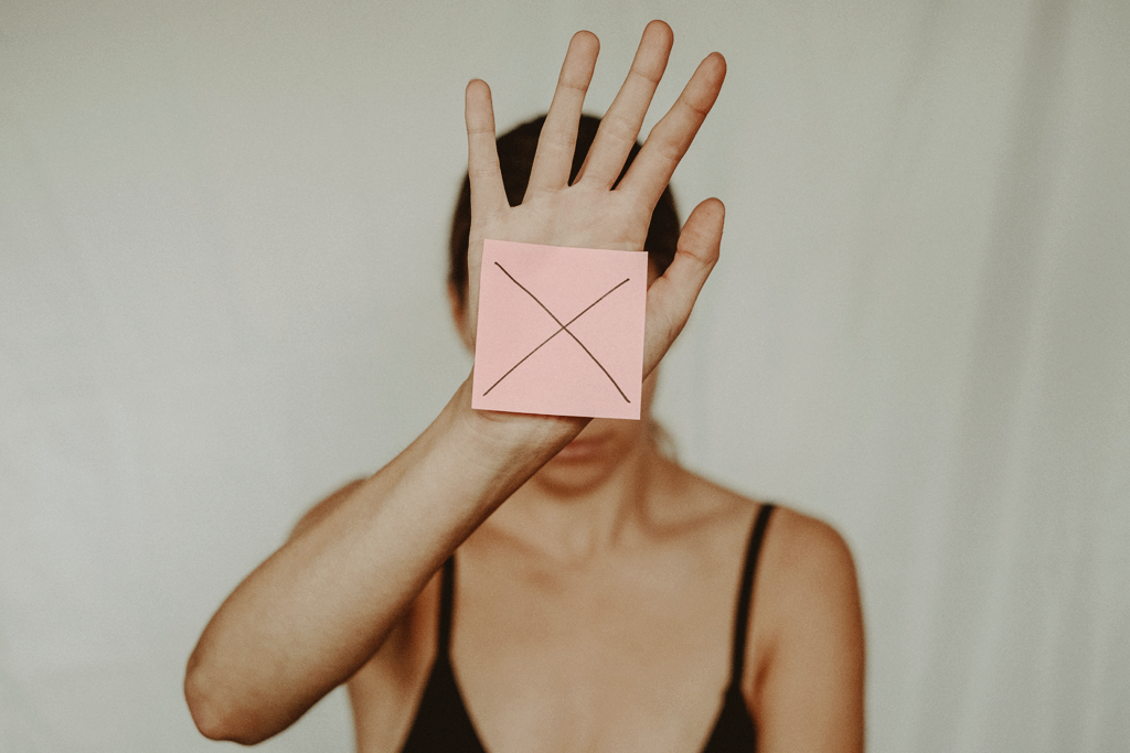 Abuse prevention. A close-up picture of a woman holding her open hand up. She's holding a pink post-it with a cross drawn on it.
