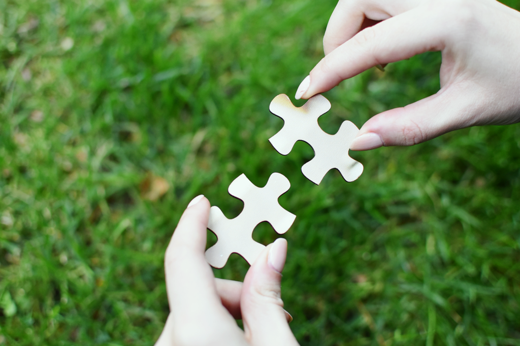 Parts Work Therapy: What does it look like? A picture of two hands holding two puzzle pieces close together, outdoors.