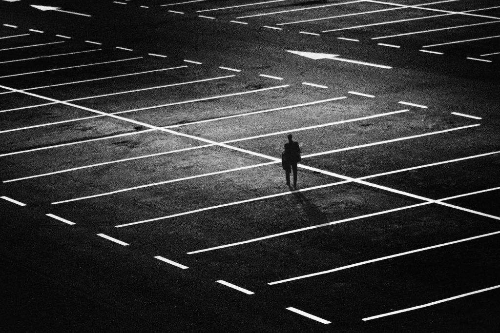 The traumatizing experience of systemic discrimination. A black and white picture of a person walking alone in an empty parking lot.