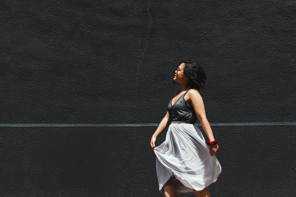 A woman walking along a grey wall background, looking content. It symbolizes a self-care practice.