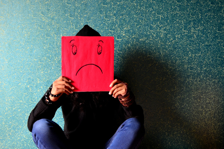 What is anxiety? Picture of a person holding a red sign with a sad face drawn on it.